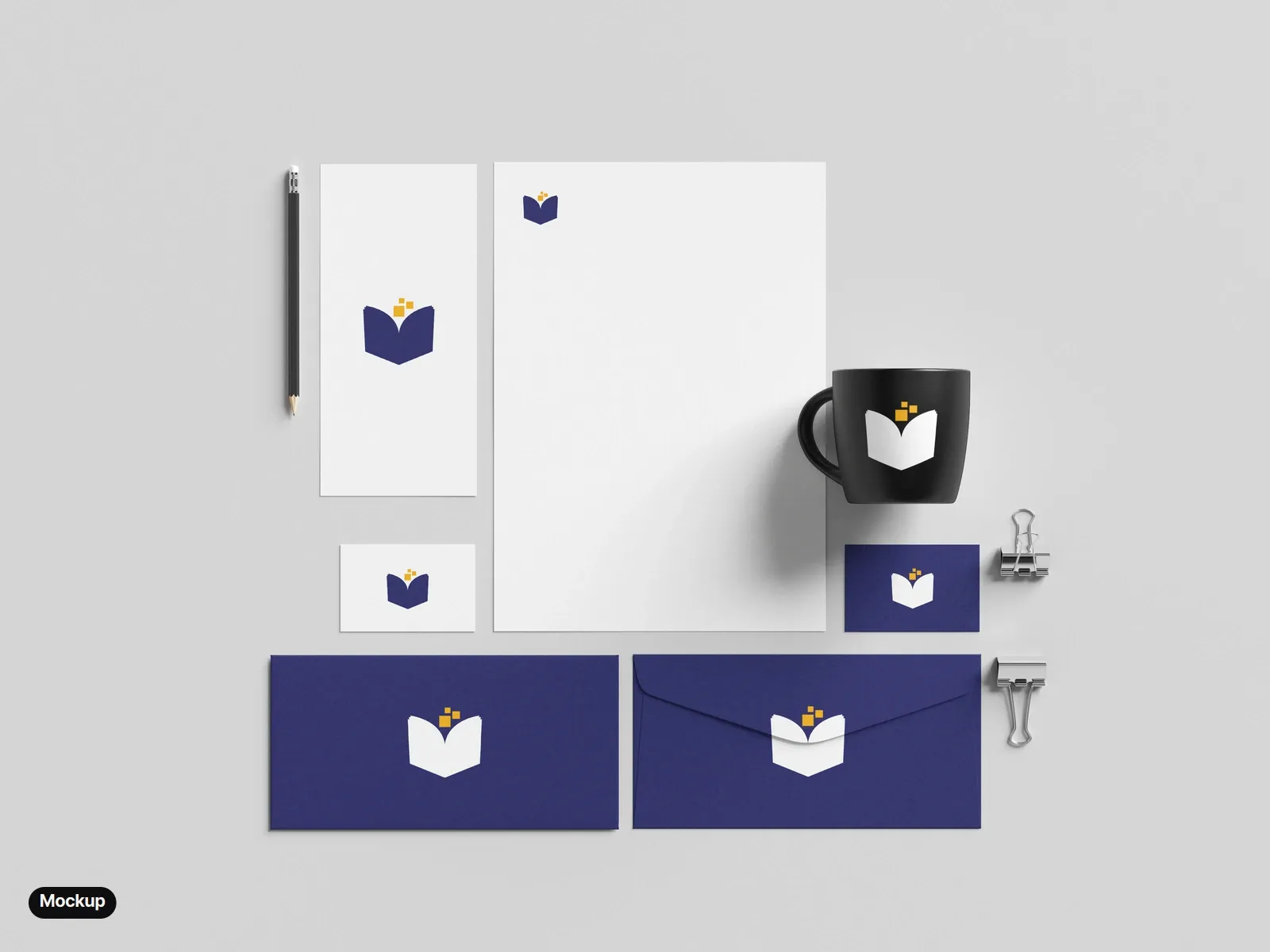 Mockup: a stationery set from above: a white letterhead, a DL card and a white business card with the full-colour mark; an indigo business card, two indigo envelopes and a black mug with the reversed mark.